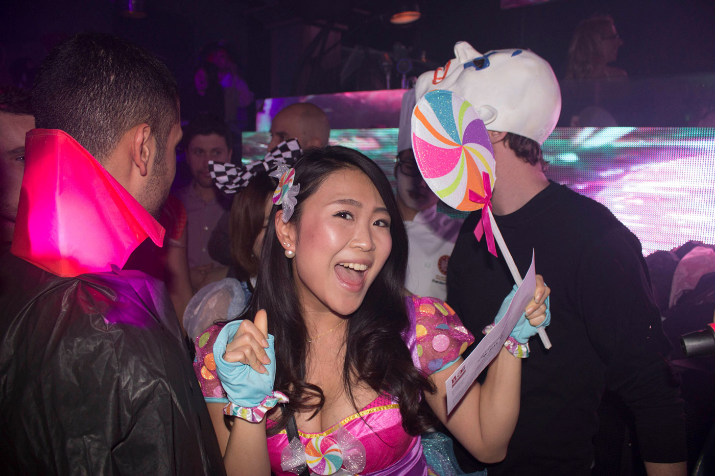 ILAC students at a theme party wearing costumes; one girl holding a lollipop prop and an ILAC letter 