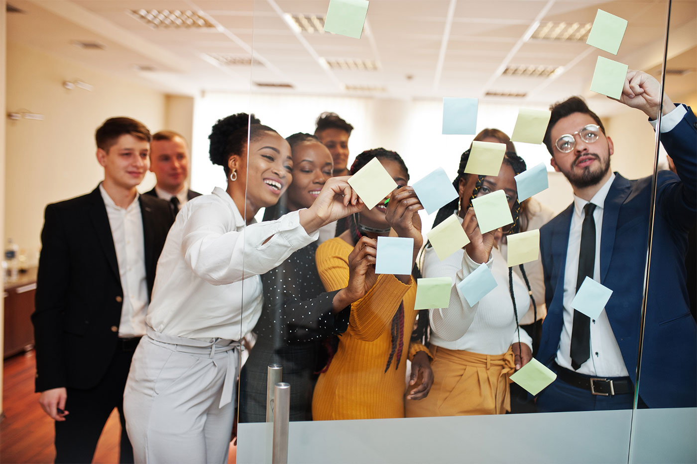 A group of business people standing in front of a glass wall with sticky notes on it
