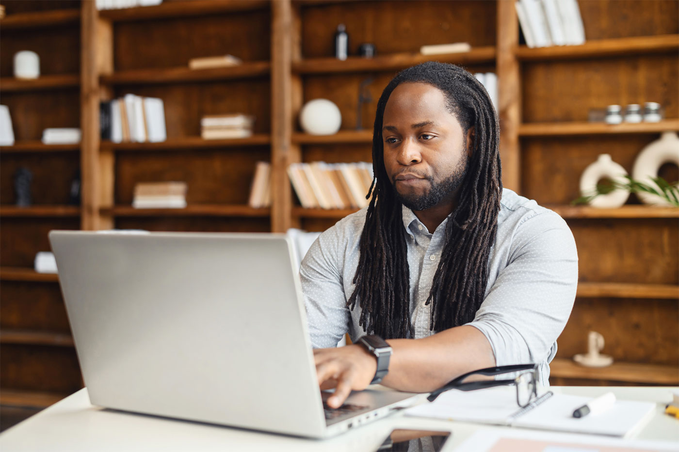 A person using a laptop in an office at a desk with a bookshelf behind them