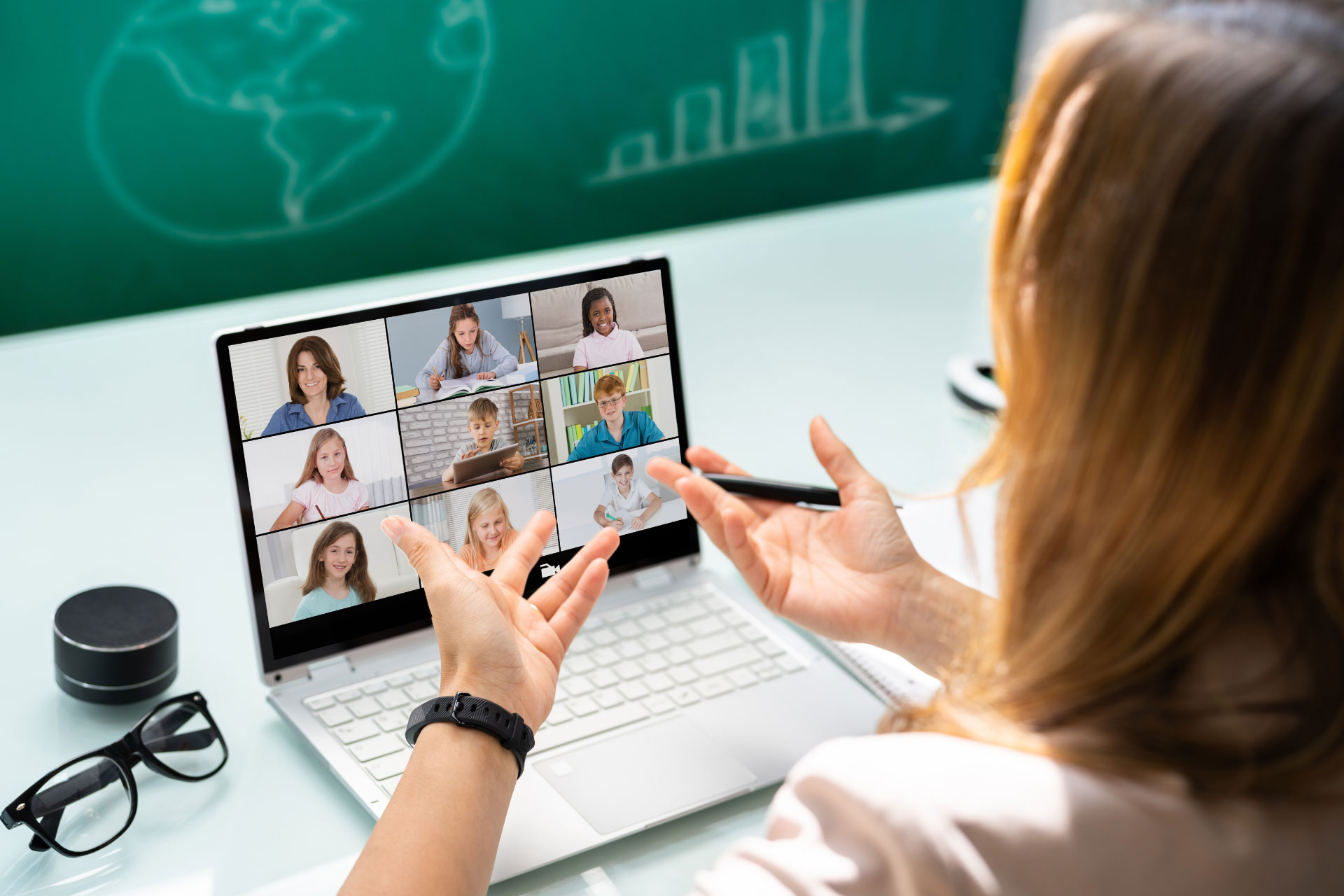 A person sitting at a desk with a laptop doing a presentation for a group of online students on the screen
