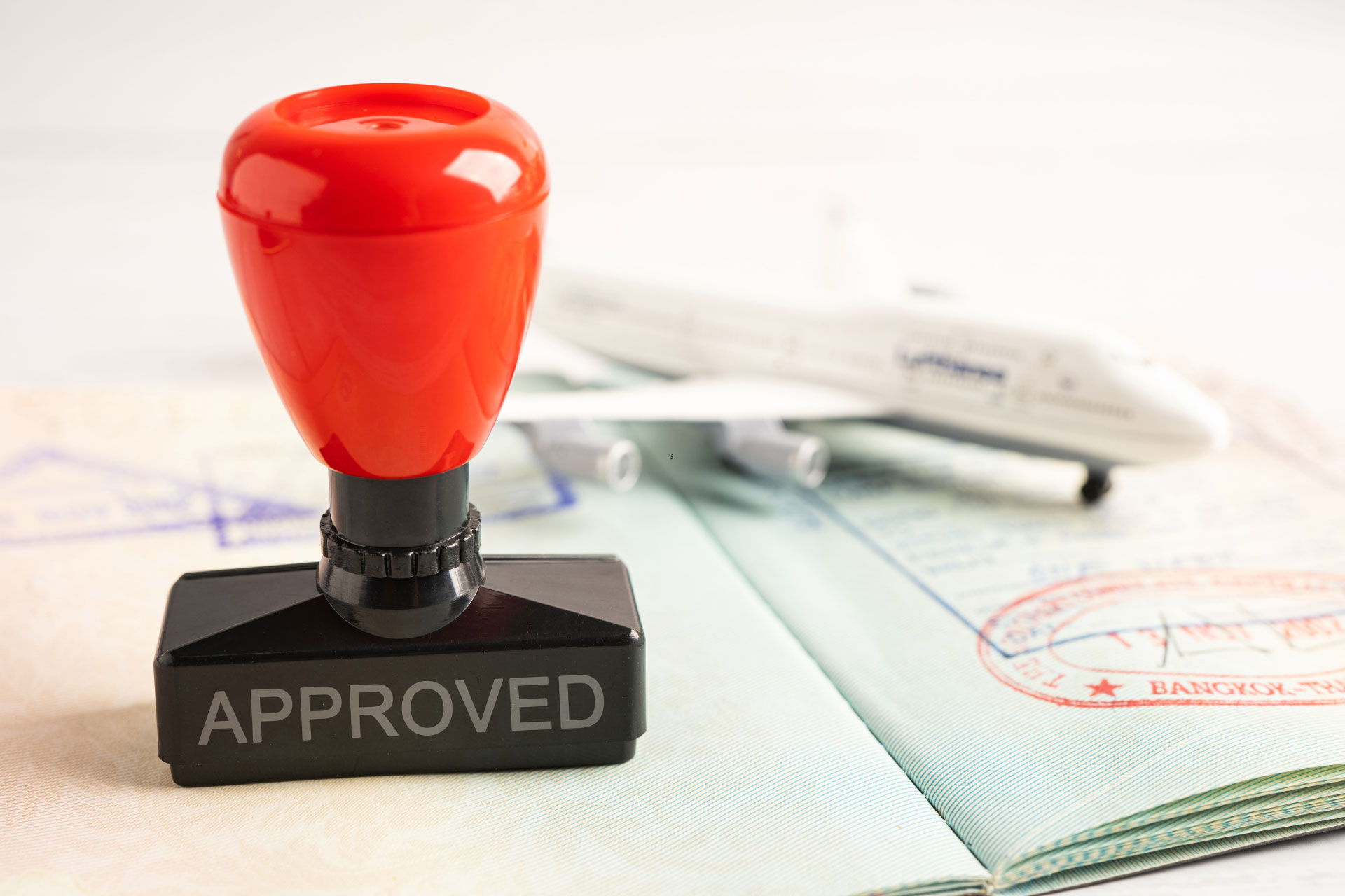 A red stamp with the word “Approved” on top of a passport next to a model airplane