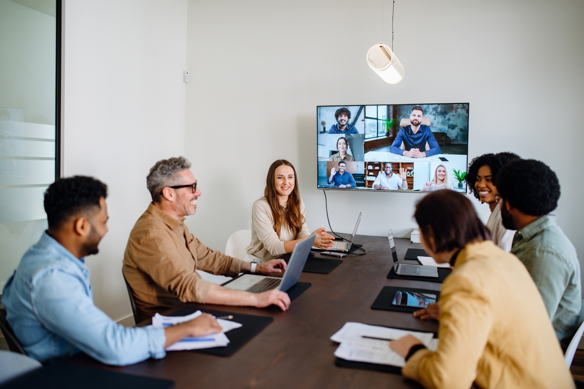Colleagues meeting in a conference room with a large screen showing remote collaborators