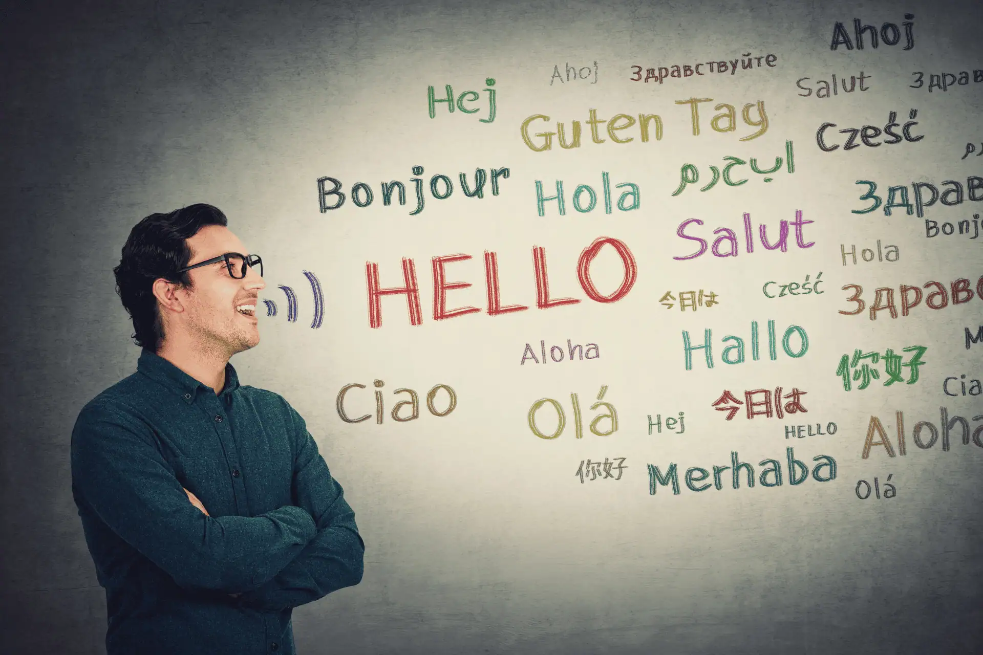 A man stands in front of a wall with “Hello” written in English and several other languages.