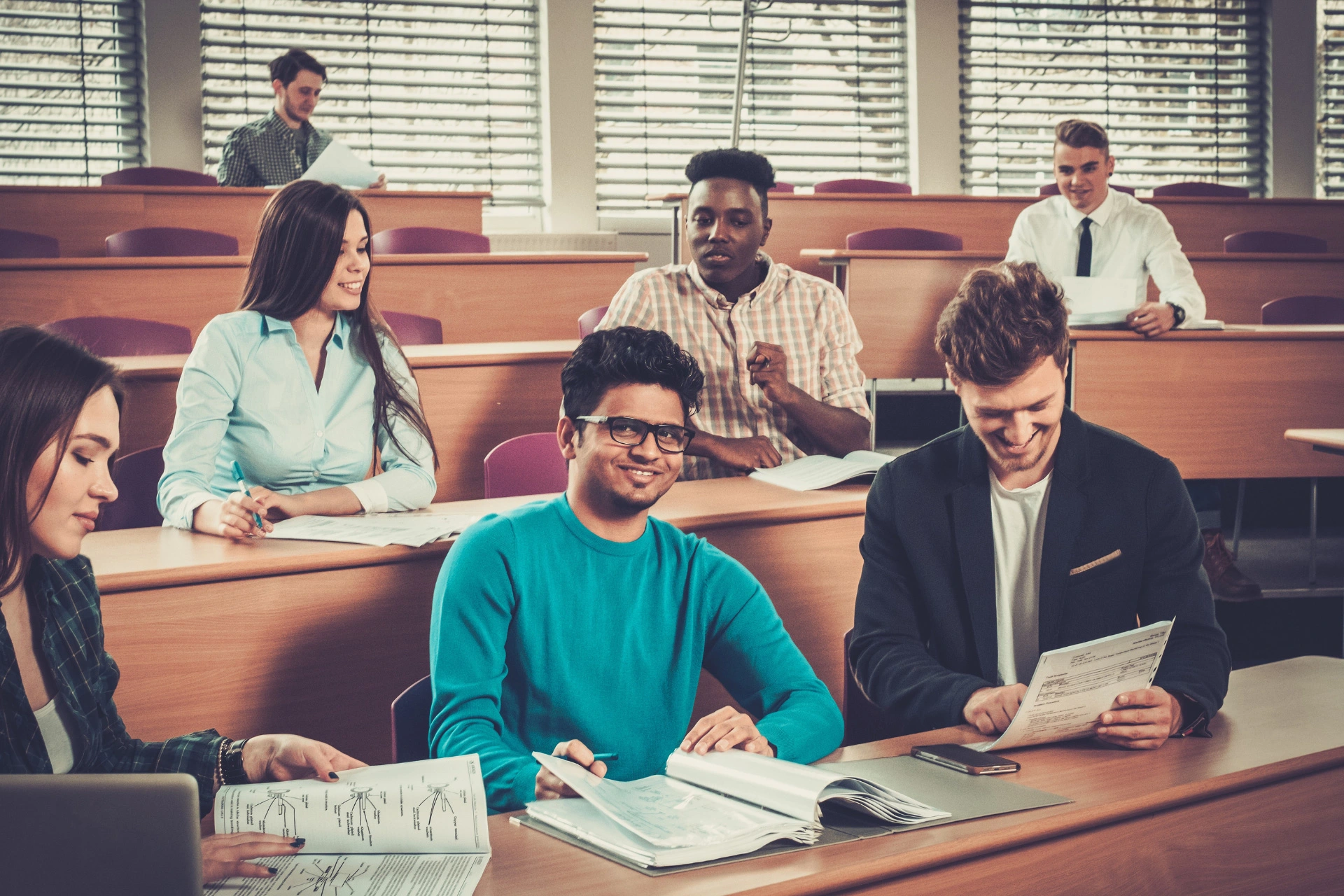 A group of happy students sit and review materials in a lecture hall.