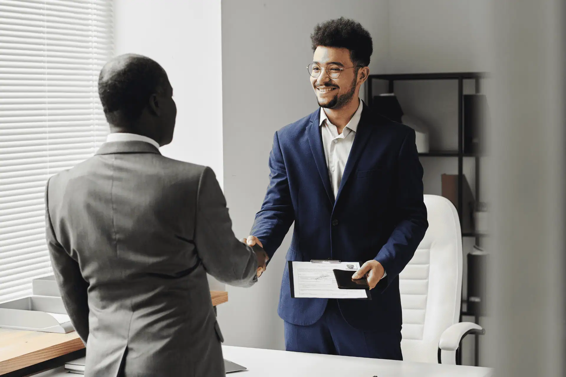 A man is congratulated by another as they shake hands, presumably for a job offer or immigration visa.
