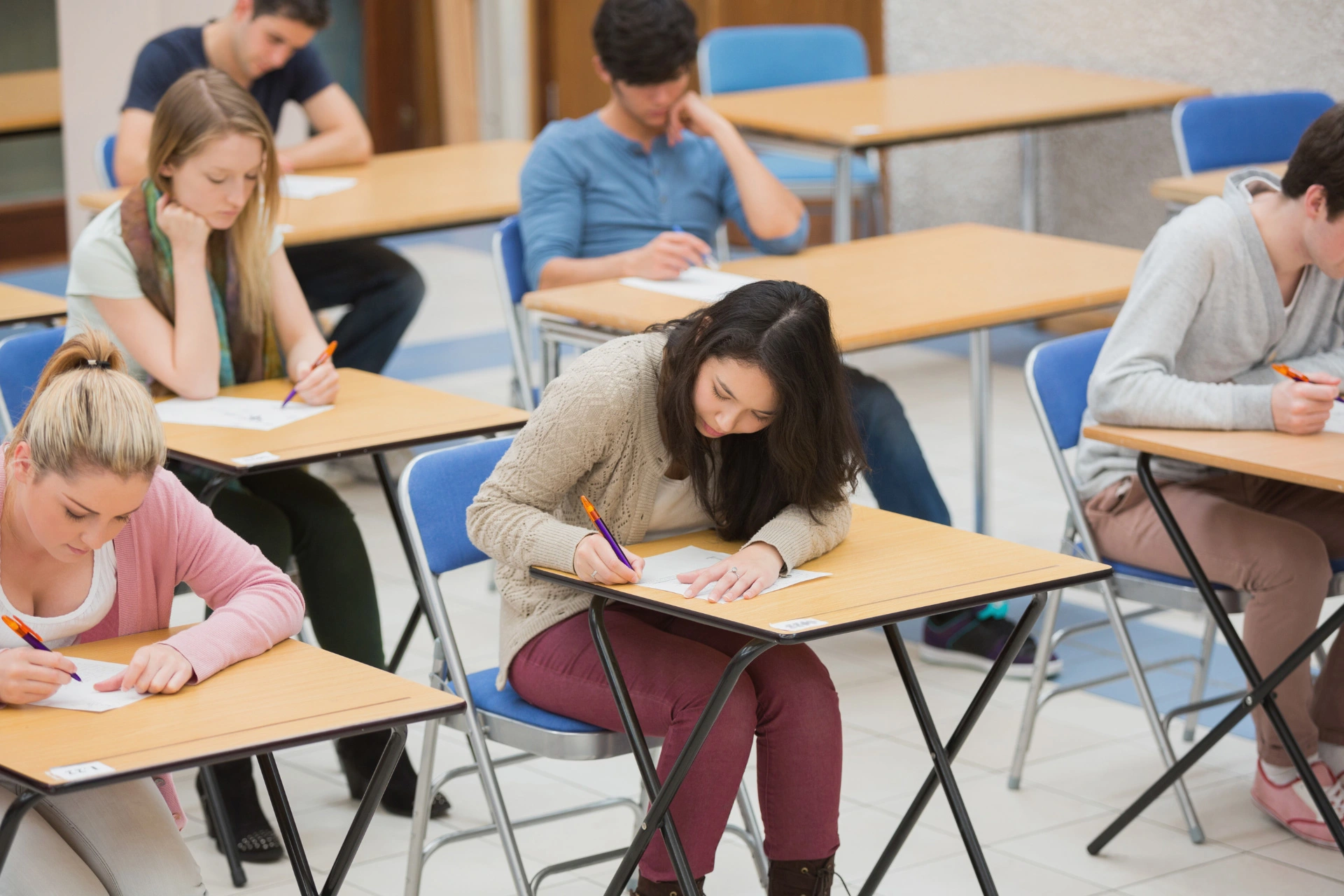 Students sit in an exam hall, writing on their test paper