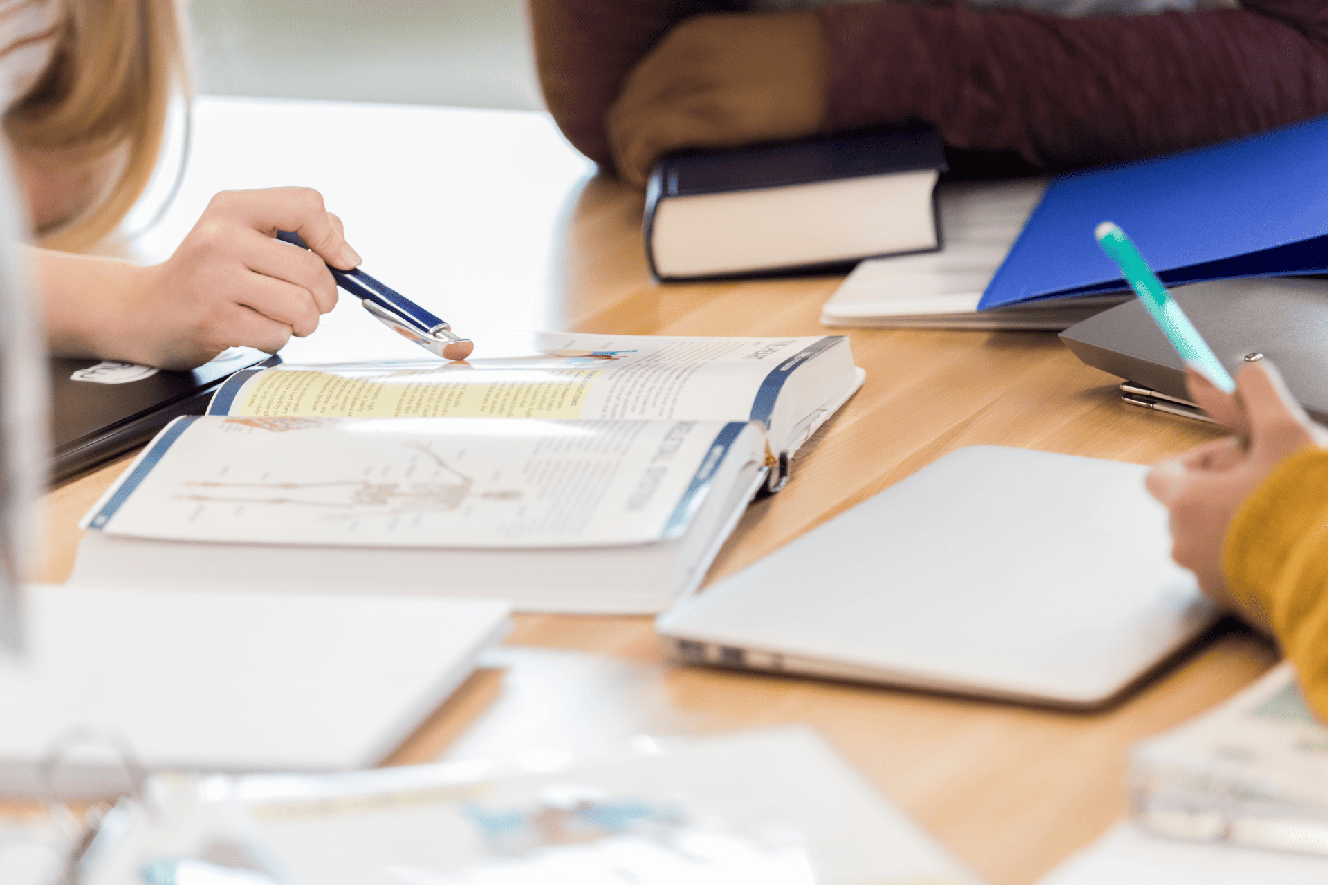 Students sit together at a table, surrounding multiple textbooks and notebooks.