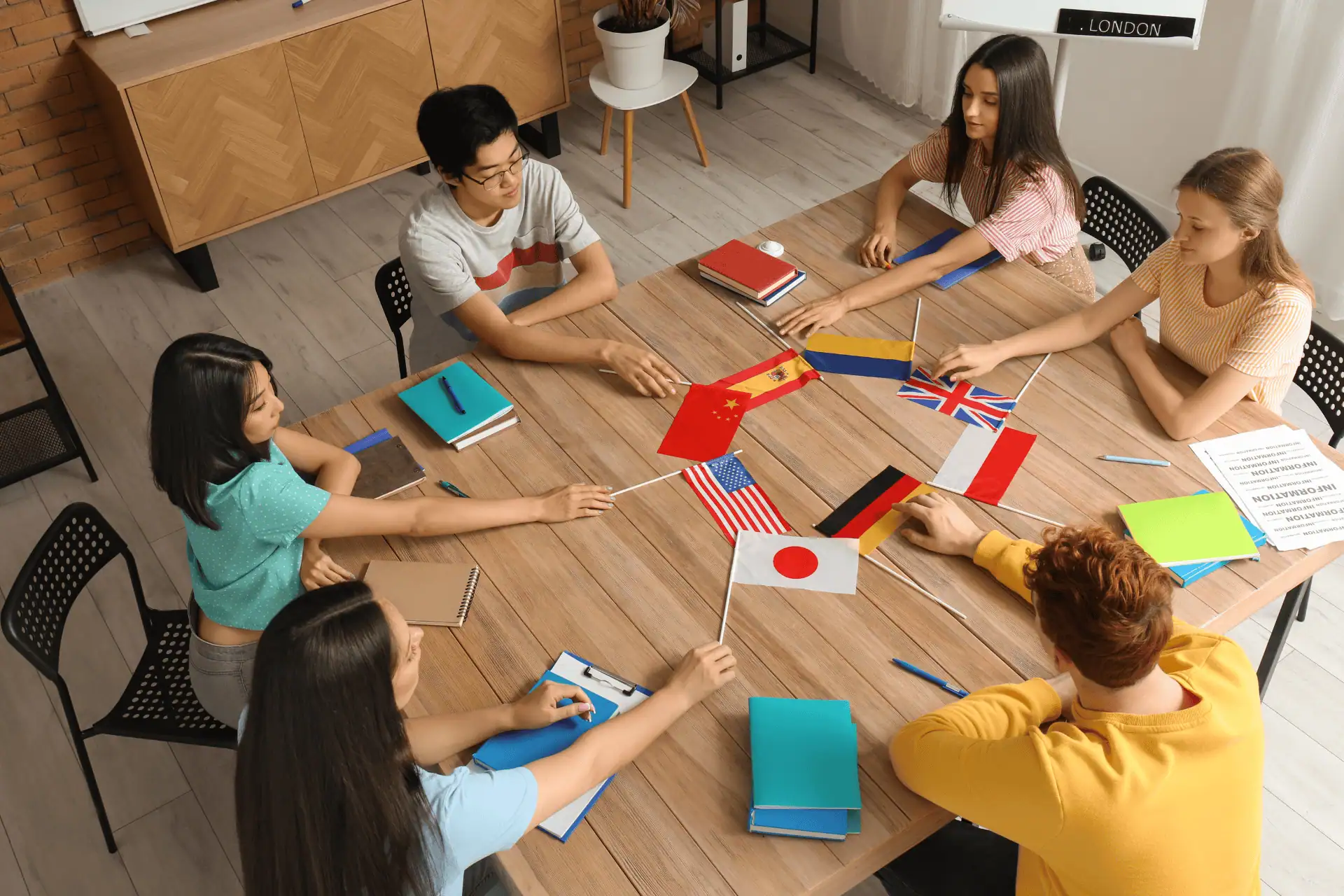 Young adult students sit at a table with textbooks and eight flags from different countries.